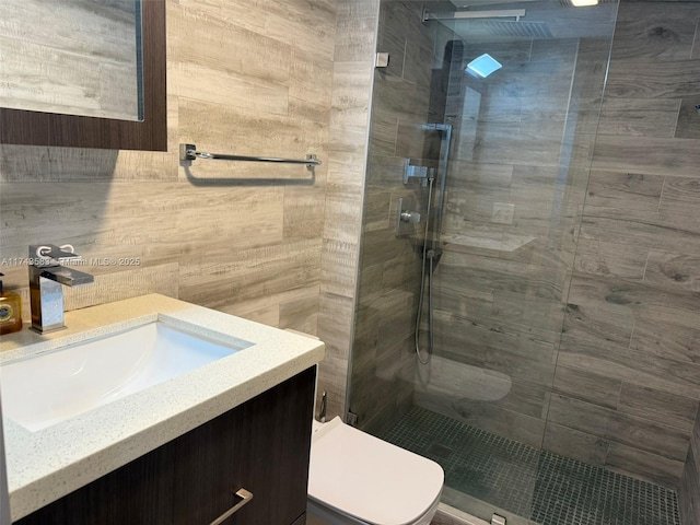 full bath with toilet, a tile shower, tile walls, and vanity