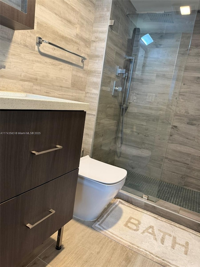 bathroom featuring wood finished floors, tiled shower, vanity, and toilet