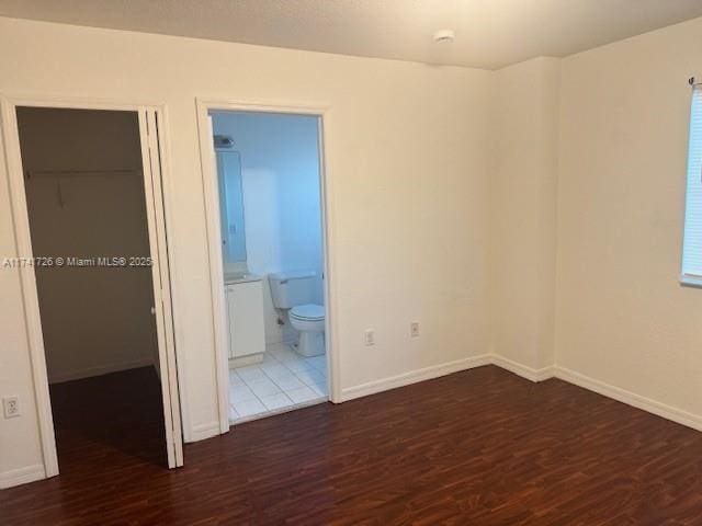 unfurnished bedroom with connected bathroom, a closet, a spacious closet, and dark hardwood / wood-style floors