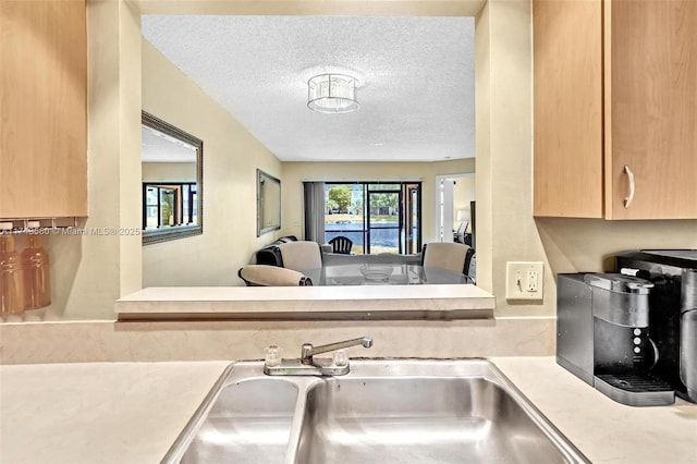 kitchen with light brown cabinetry, sink, and a textured ceiling