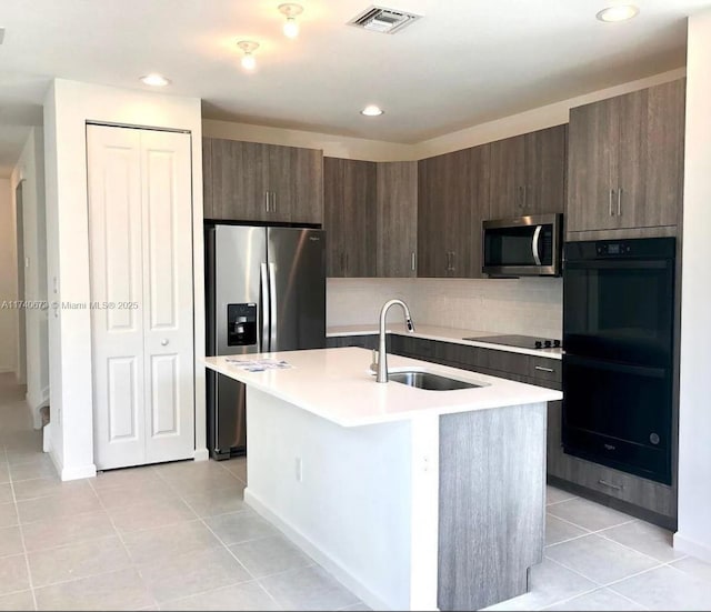 kitchen featuring dark brown cabinetry, sink, black appliances, a kitchen island with sink, and backsplash