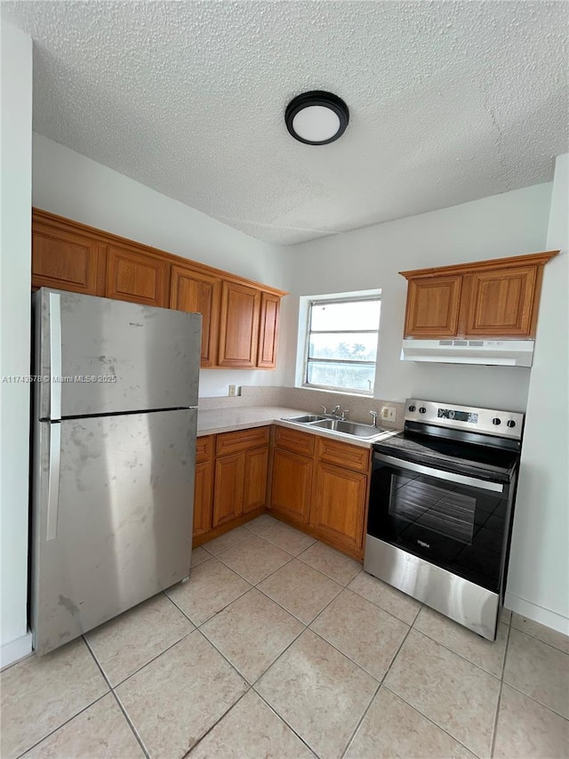 kitchen with stainless steel appliances, sink, light tile patterned floors, and a textured ceiling