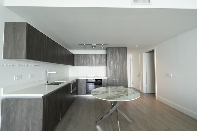 kitchen with dishwasher, rail lighting, sink, kitchen peninsula, and light wood-type flooring