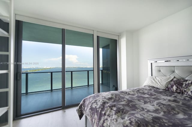 bedroom with hardwood / wood-style flooring, a water view, access to outside, and a wall of windows