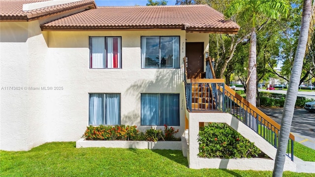 back of property featuring a tiled roof, stairway, a lawn, and stucco siding