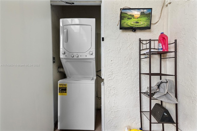 laundry area with a textured wall, laundry area, and stacked washer / drying machine