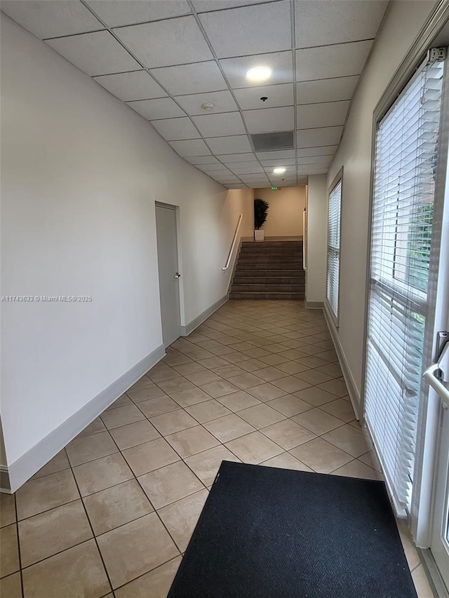 hallway featuring stairway, light tile patterned floors, baseboards, and a drop ceiling