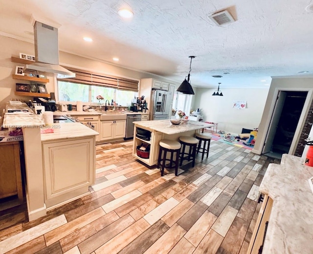 kitchen featuring appliances with stainless steel finishes, a kitchen breakfast bar, island range hood, a kitchen island, and decorative light fixtures