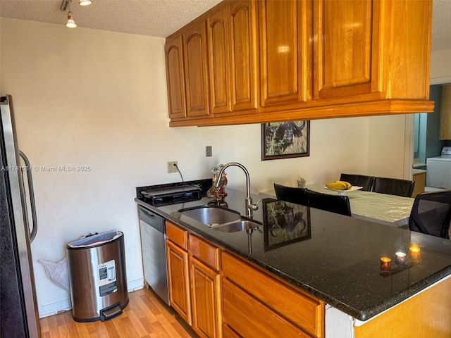 kitchen with sink, appliances with stainless steel finishes, dark stone countertops, a textured ceiling, and light wood-type flooring