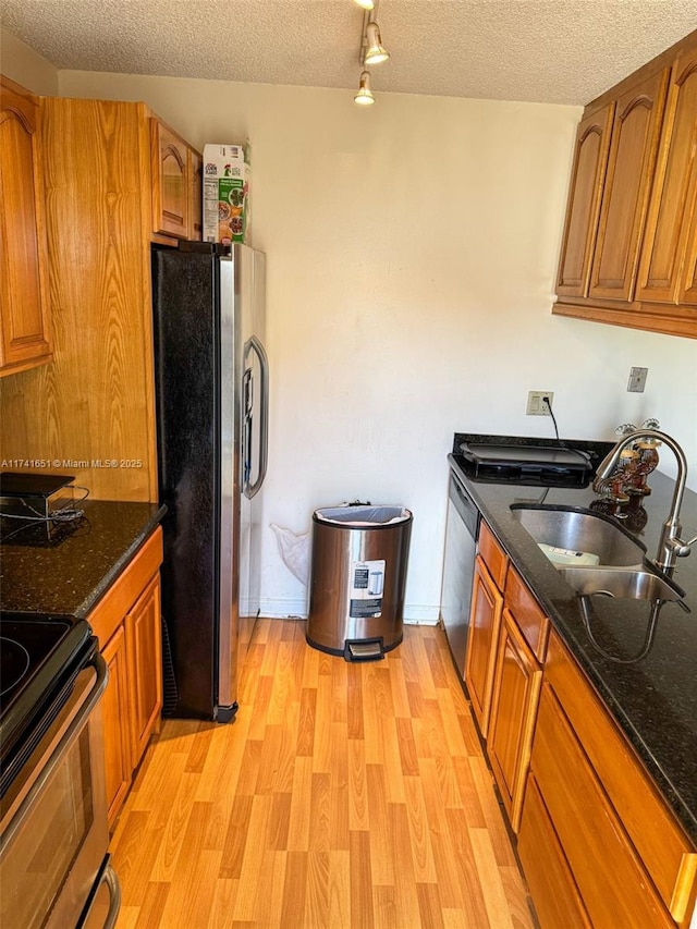 kitchen with stainless steel appliances, sink, light hardwood / wood-style flooring, and dark stone countertops