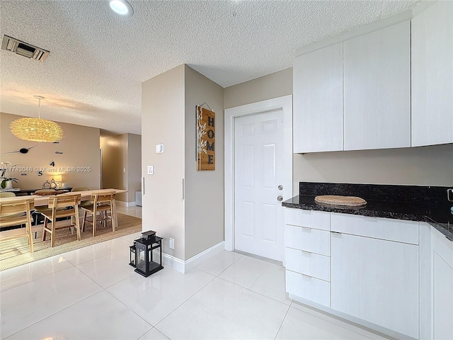 kitchen featuring a textured ceiling, light tile patterned floors, white cabinetry, and visible vents