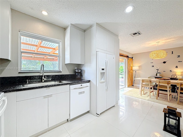 kitchen with white appliances, a textured ceiling, visible vents, a barn door, and a sink