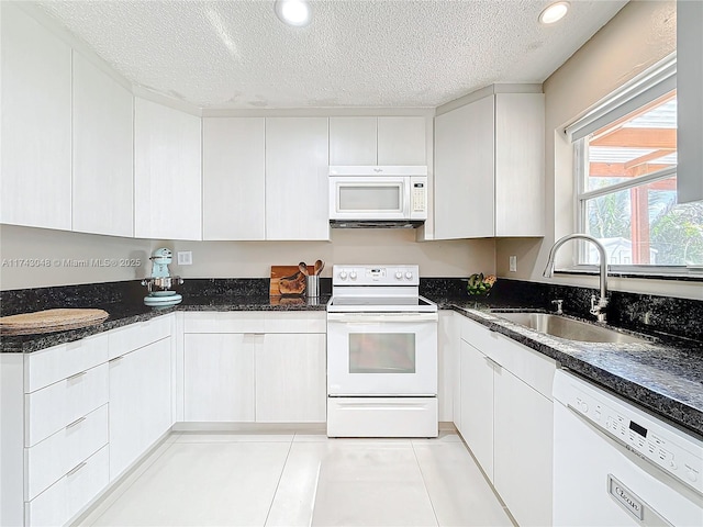 kitchen with dark stone counters, white appliances, a textured ceiling, white cabinetry, and a sink