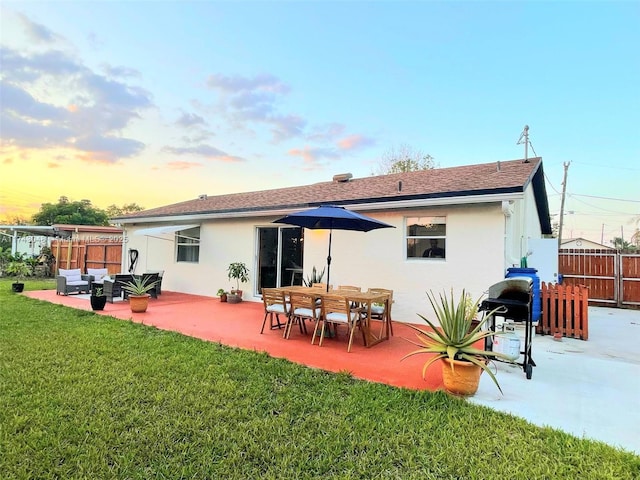 back of house at dusk featuring a yard, fence, a patio, an outdoor hangout area, and stucco siding