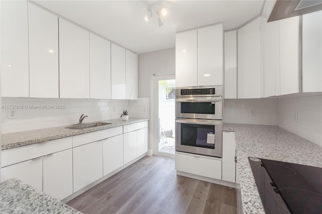 kitchen with sink, light stone counters, black electric stovetop, white cabinets, and stainless steel double oven