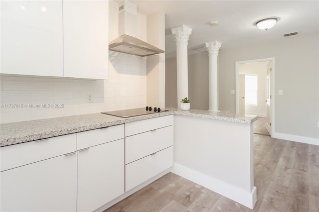 kitchen featuring wall chimney range hood, decorative columns, tasteful backsplash, white cabinets, and kitchen peninsula