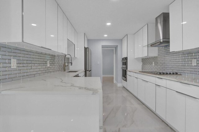 kitchen with appliances with stainless steel finishes, sink, white cabinets, light stone countertops, and wall chimney range hood