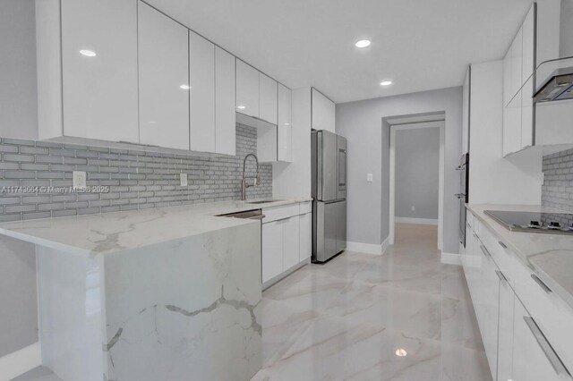 kitchen with stainless steel refrigerator, white cabinetry, sink, light stone countertops, and black electric cooktop