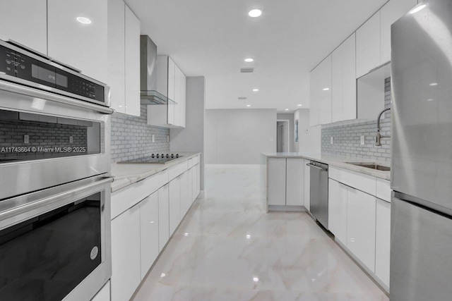 kitchen with sink, appliances with stainless steel finishes, light stone counters, white cabinets, and wall chimney exhaust hood