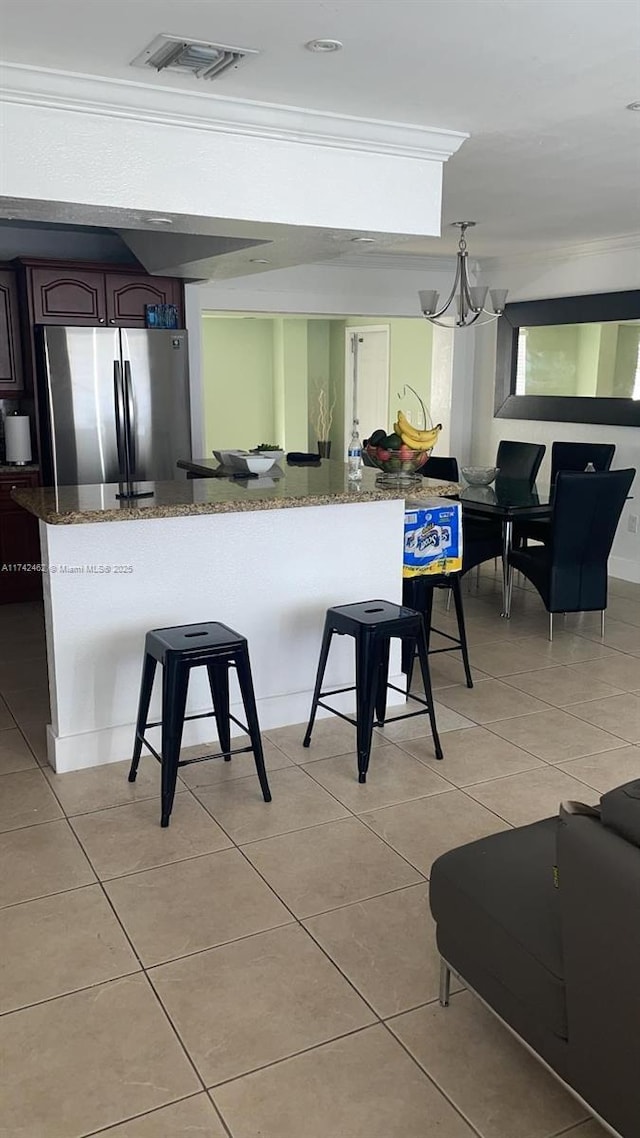 kitchen featuring dark stone countertops, a breakfast bar area, stainless steel fridge, a chandelier, and ornamental molding