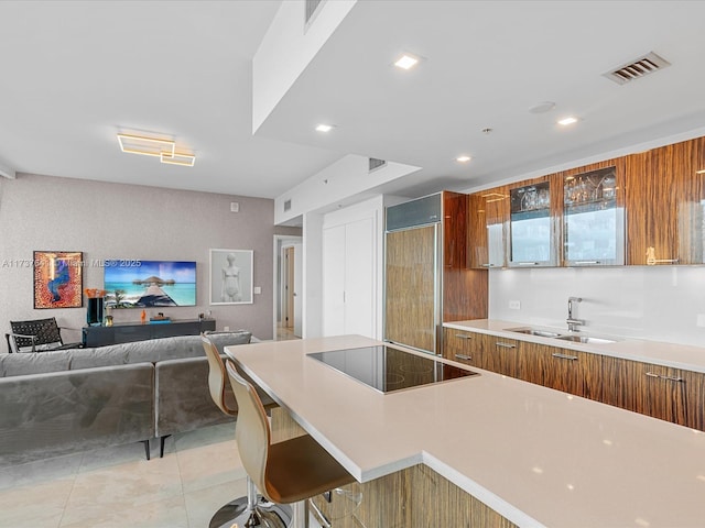 kitchen with a kitchen bar, sink, light tile patterned flooring, paneled refrigerator, and black electric cooktop