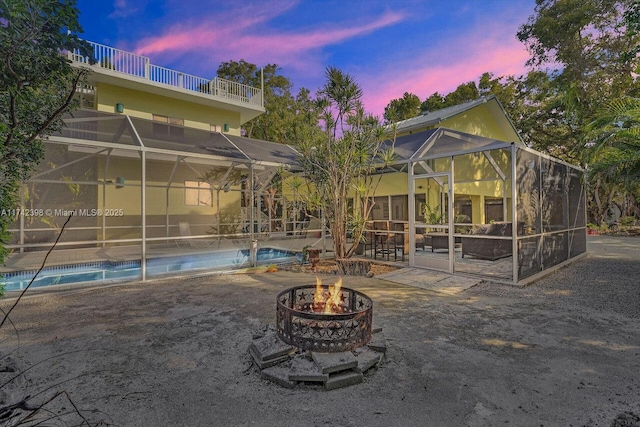 back of property at dusk with an outdoor fire pit, a patio area, and a lanai