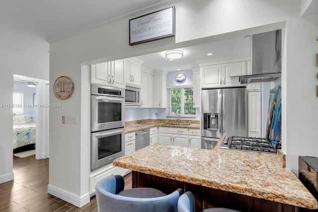 kitchen featuring a peninsula, stainless steel appliances, crown molding, a kitchen bar, and white cabinetry