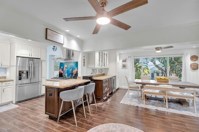 kitchen featuring stainless steel appliances, white cabinets, wall chimney range hood, a center island, and glass insert cabinets