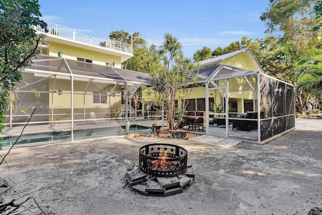 back of property with glass enclosure, an outdoor fire pit, a patio area, and an outdoor pool