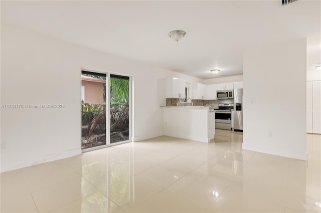 interior space featuring light tile patterned floors, appliances with stainless steel finishes, white cabinetry, decorative backsplash, and kitchen peninsula