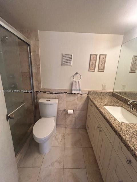 bathroom featuring vanity, toilet, an enclosed shower, and tile walls