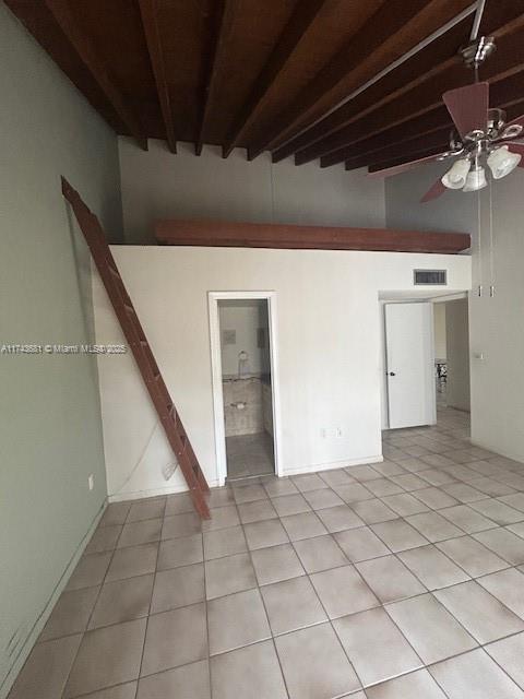 tiled empty room with beamed ceiling and ceiling fan