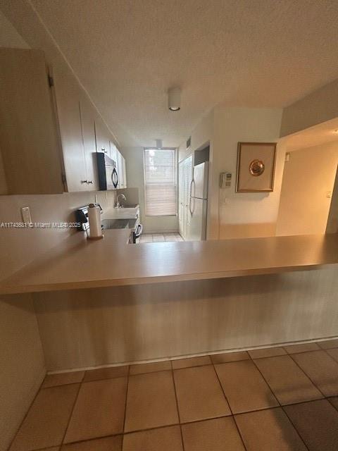 kitchen featuring tile patterned flooring, white cabinetry, white fridge, and a textured ceiling