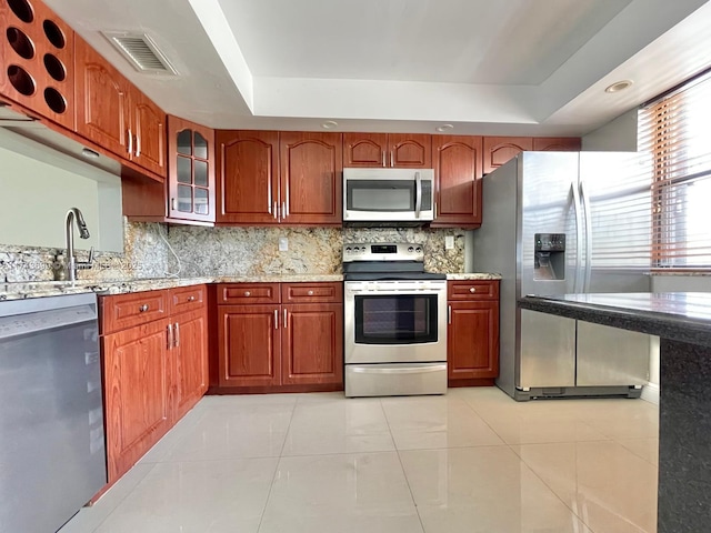 kitchen with a raised ceiling, appliances with stainless steel finishes, sink, and backsplash