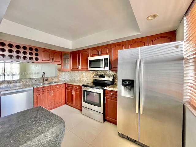 kitchen featuring appliances with stainless steel finishes, tasteful backsplash, sink, light tile patterned floors, and a tray ceiling