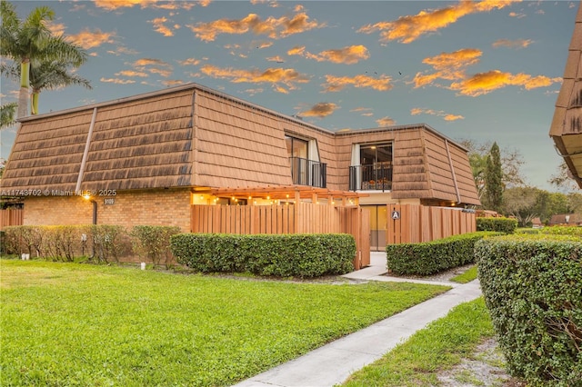 property exterior at dusk featuring a lawn and a balcony