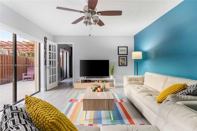 living room featuring ceiling fan, light hardwood / wood-style flooring, french doors, and a textured ceiling