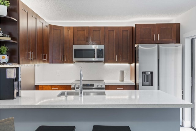 kitchen with sink, a kitchen bar, kitchen peninsula, stainless steel appliances, and a textured ceiling