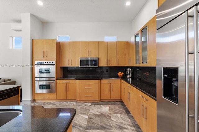 kitchen featuring appliances with stainless steel finishes, dark stone countertops, light brown cabinetry, and decorative backsplash