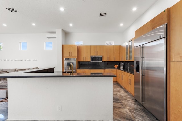 kitchen featuring appliances with stainless steel finishes, tasteful backsplash, sink, a wall mounted AC, and a kitchen island with sink