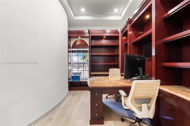 office area with built in desk, a raised ceiling, and light hardwood / wood-style flooring