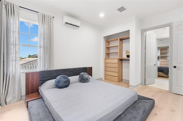 bedroom with a wall mounted air conditioner, a spacious closet, light hardwood / wood-style floors, and a closet