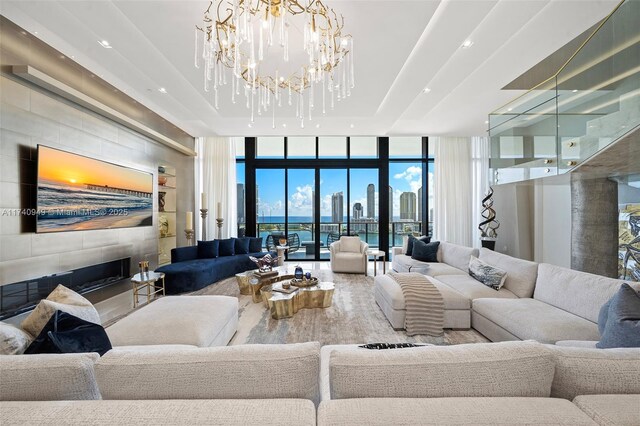 living area with expansive windows, wood finished floors, a tiled fireplace, a raised ceiling, and a notable chandelier