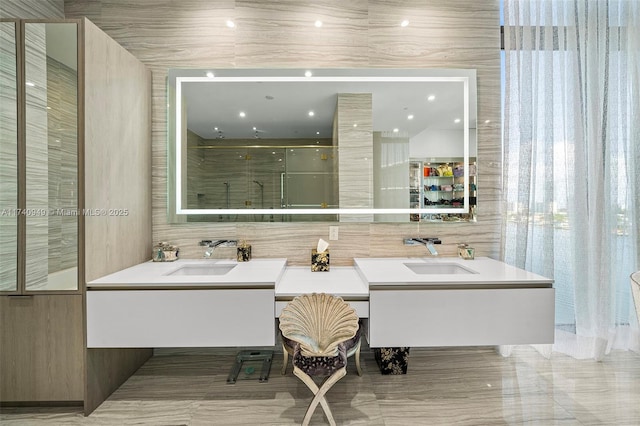 full bath featuring walk in shower, double vanity, a sink, and tile walls
