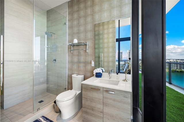 bathroom featuring vanity, toilet, a shower stall, a water view, and tile walls