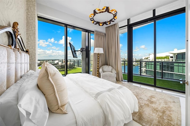 bedroom with a water view, access to exterior, a notable chandelier, and a wall of windows