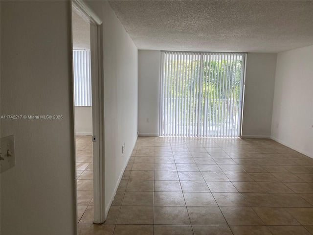 unfurnished room with light tile patterned flooring, a wall of windows, and a textured ceiling