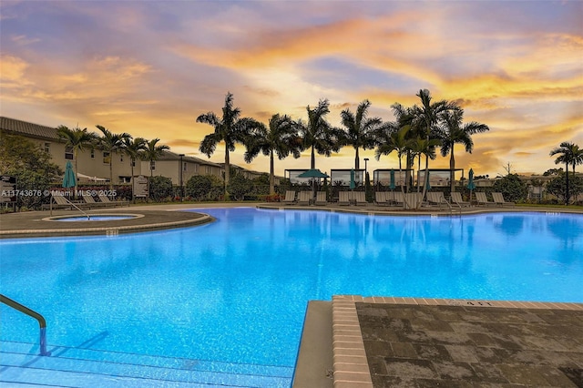 pool at dusk with a patio area and a hot tub