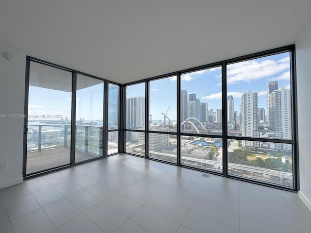 tiled empty room featuring floor to ceiling windows, a city view, and baseboards