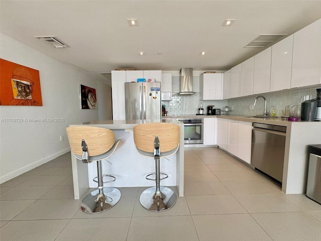 kitchen with wall chimney range hood, a sink, visible vents, and appliances with stainless steel finishes